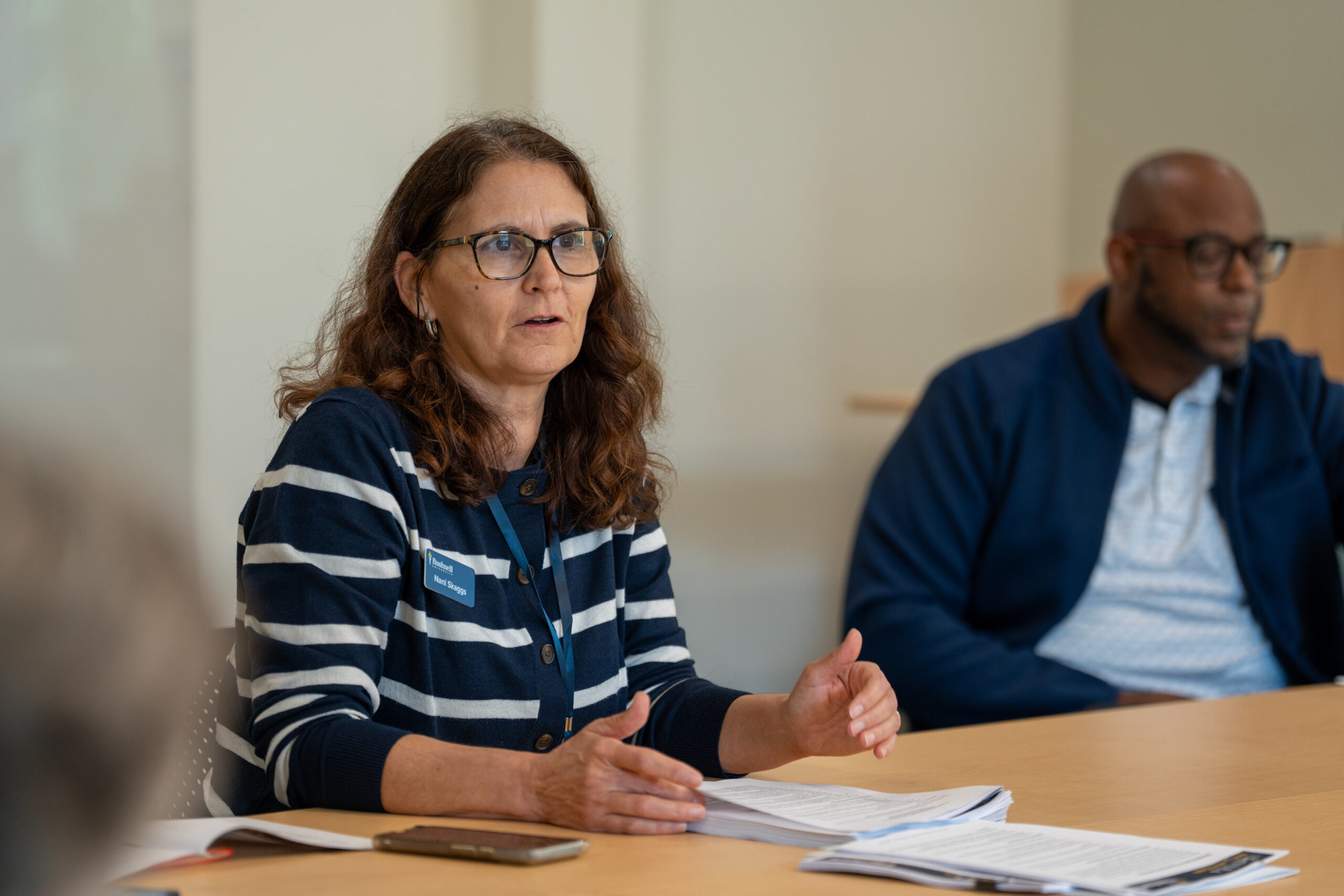 A woman seated at a table and speaking to someone off camera.